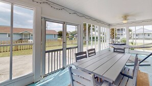 A covered patio with a table and chairs, large windows, and a hammock.