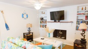 A living room with a sofa, coffee table, fireplace, bookshelf, and a mounted TV.