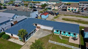 A coastal hotel with a blue roof, a fenced patio, and a view of the beach and pier.