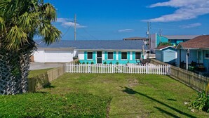 A coastal house with a white picket fence, a small yard, and a clear blue sky.