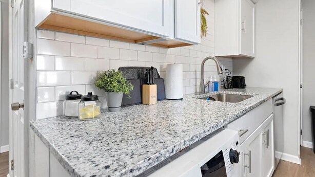 Una cocina moderna con armarios blancos, encimeras de granito y un lavamanos de acero inoxidable.