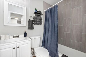 A bathroom with a white sink, a toilet, a blue shower curtain, and a towel rack with folded towels.
