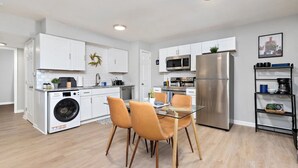 Una cocina moderna con armarios blancos, electrodomésticos de acero inoxidable y una mesa de comedor de vidrio con sillas.