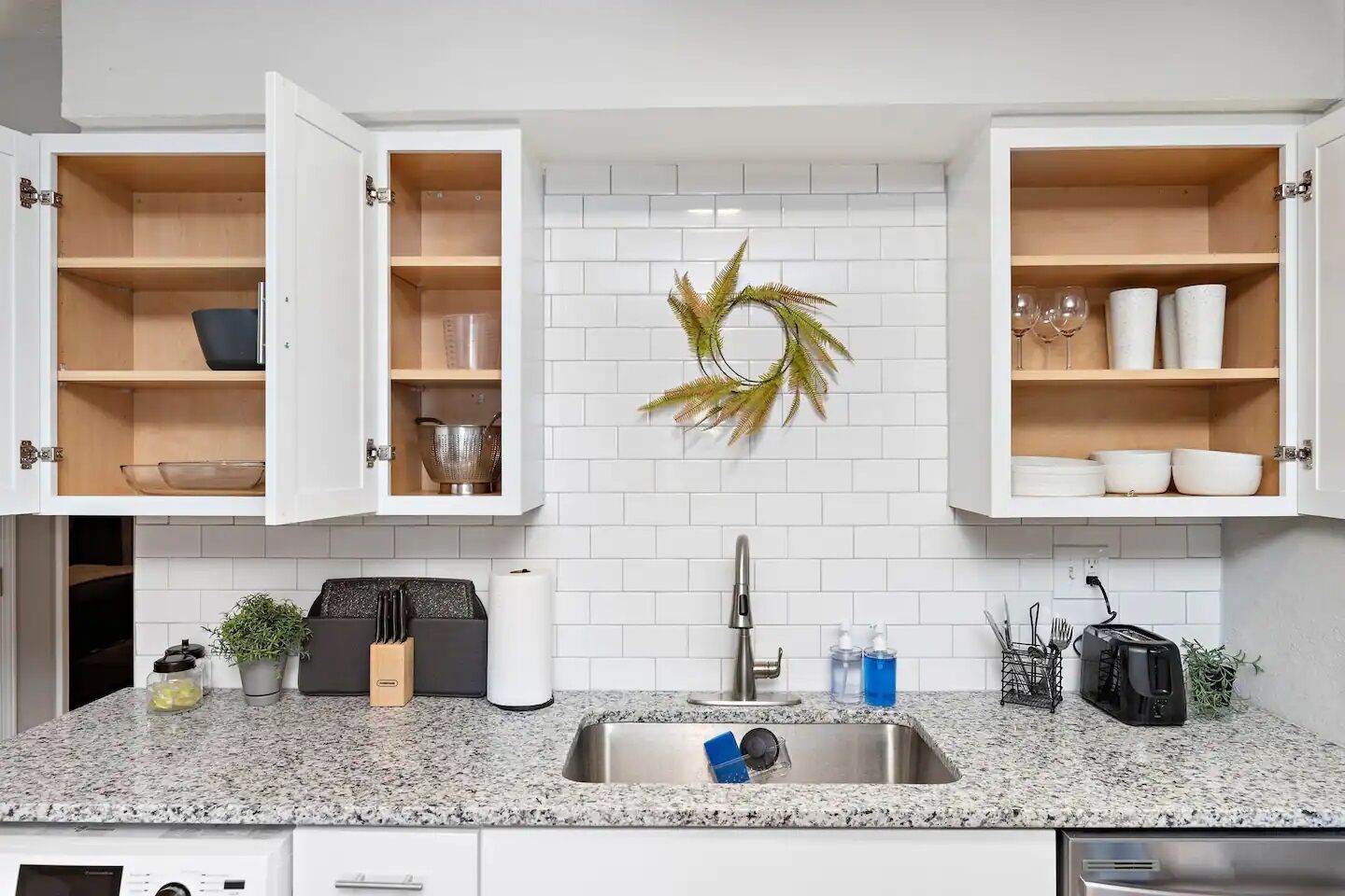 Una cocina moderna con encimeras de granito, armarios blancos y un lavamanos de acero inoxidable.