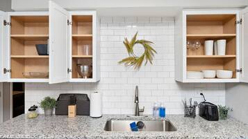 Una cocina moderna con encimeras de granito, armarios blancos y un lavamanos de acero inoxidable.