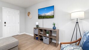 Una sala de estar moderna con una consola de madera, una lámpara de pie y un televisor montado que muestra un paisaje.