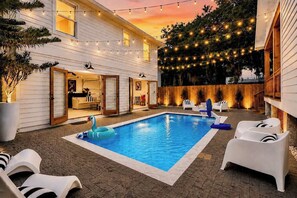 Una piscina con sillas de descanso, luces colgantes y un cerco de madera.
