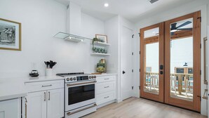 Une cuisine moderne avec des meubles blancs, un four encastré et une porte en bois donnant sur un balcon.