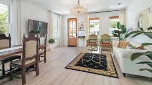 Un salon spacieux agrémenté d’un lustre, d’une table à manger avec des chaises, d’un canapé et de grandes fenêtres.