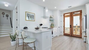 Une cuisine moderne dotée d’un îlot central, de meubles blancs et d’une porte en bois donnant sur un balcon.