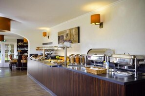 Relax in our spacious lobby, featuring a central buffet area with a variety of food options and a seating area with chairs and a table.