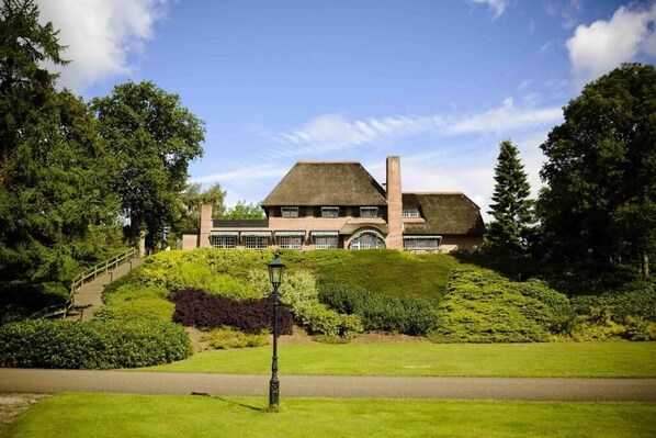 Situated on a lush hillside, this traditional building features a stately facade, multiple windows, and a charming chimney.