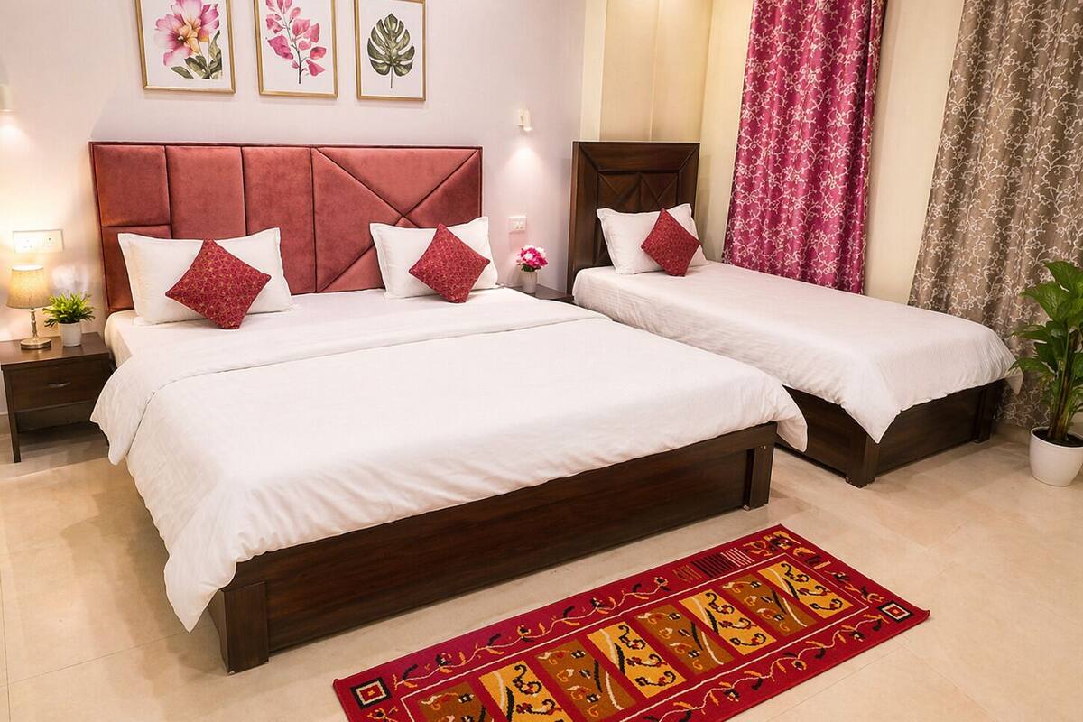 A hotel room with two beds, a red headboard, white bedding, a red and yellow patterned rug, and framed floral artwork on the wall.