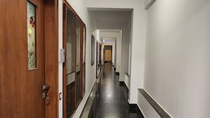 A long, narrow hallway with wooden doors on one side and a black tiled floor. - Royal Residency (Tiruvannamalai)