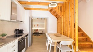 A modern kitchen with white cabinetry, a built-in oven, and a dining area with a wooden table and white chairs. - Old Town Charm – Cozy 2BR with Rooftop Terrace (Rethymno)