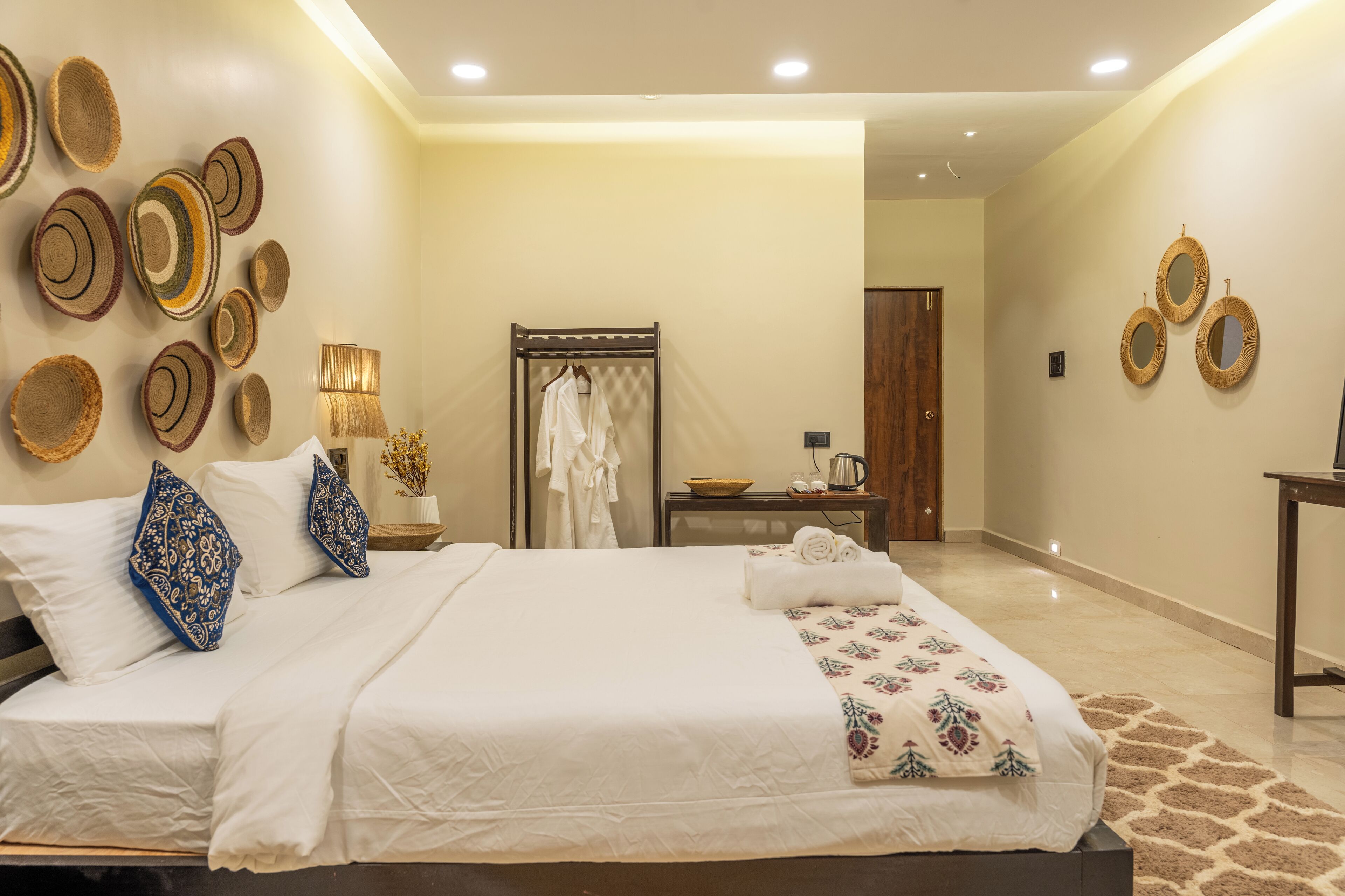 A neatly arranged hotel room with a large bed, a bedside table with a lamp, a mirror, and a wall decorated with circular woven art pieces.