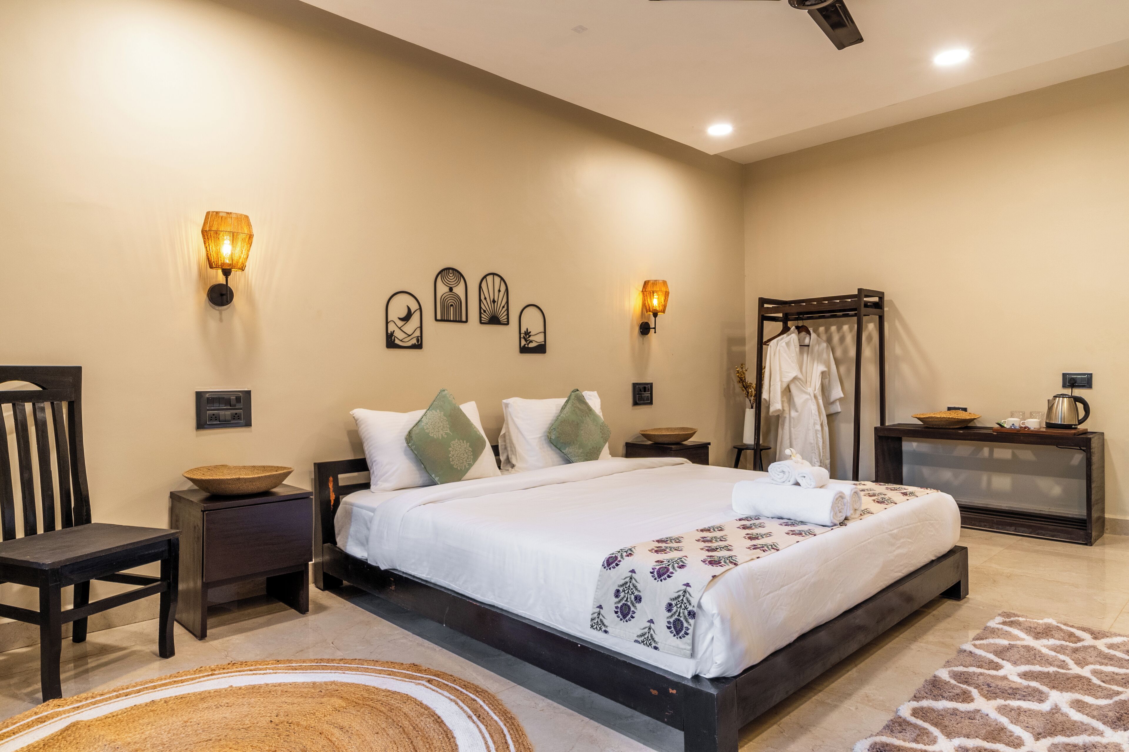 A bedroom with a large bed, bedside tables, wall-mounted lamps, a wooden chair, and a clothing rack.