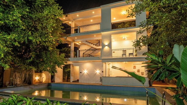 Ein mehrgeschossiges Hotel mit Schwimmbad, Balkonen und Innenbeleuchtung.