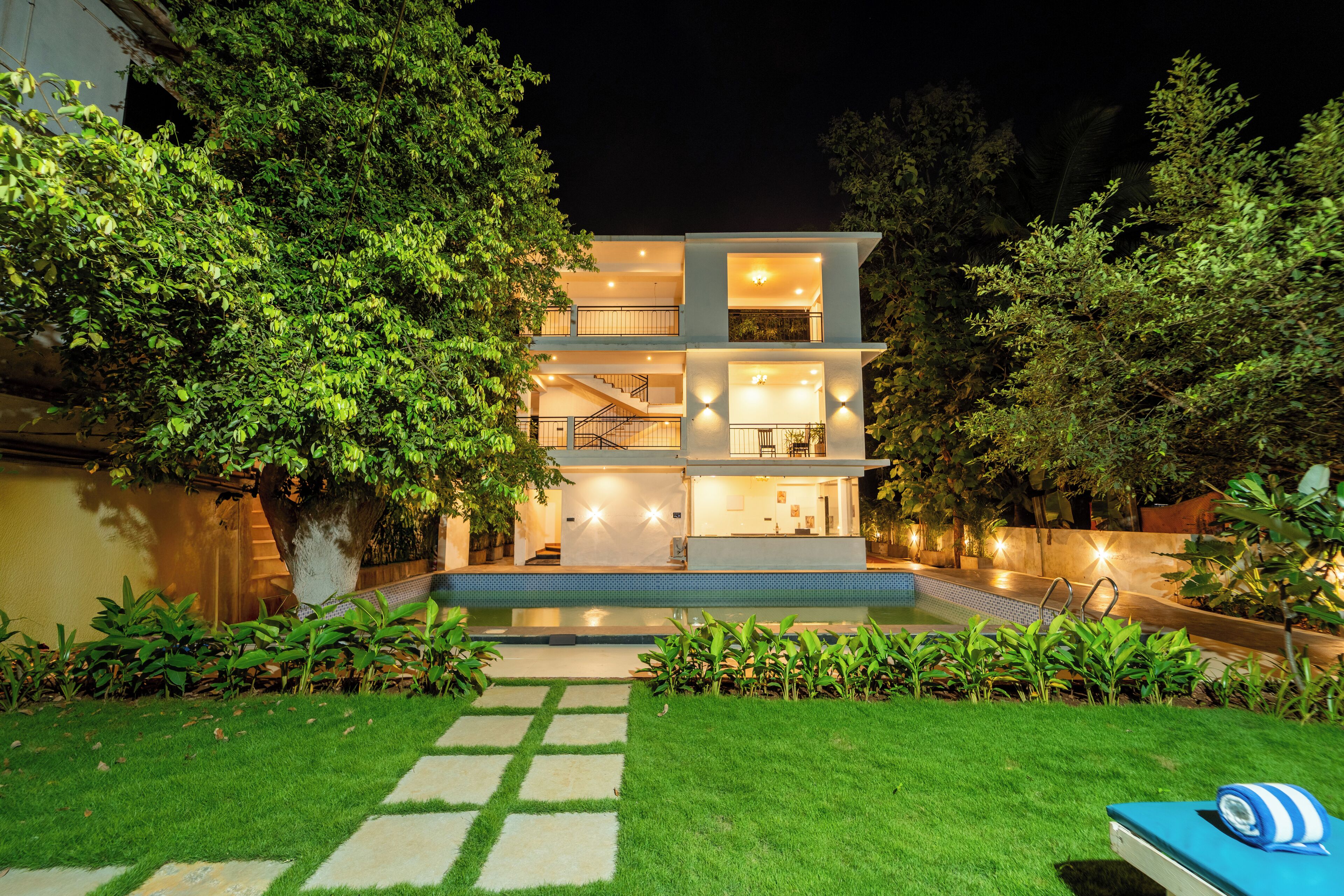 A modern multi-story house with a swimming pool, surrounded by lush greenery.