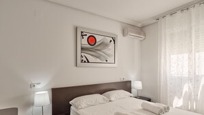 Habitación de hotel con una cama, dos mesitas de noche, aire acondicionado de pared y una ventana con cortinas translúcidas.