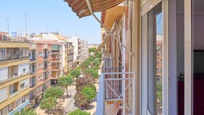 Un balcón con vistas a una calle arbolada, una barandilla metálica y un edificio de varios pisos.