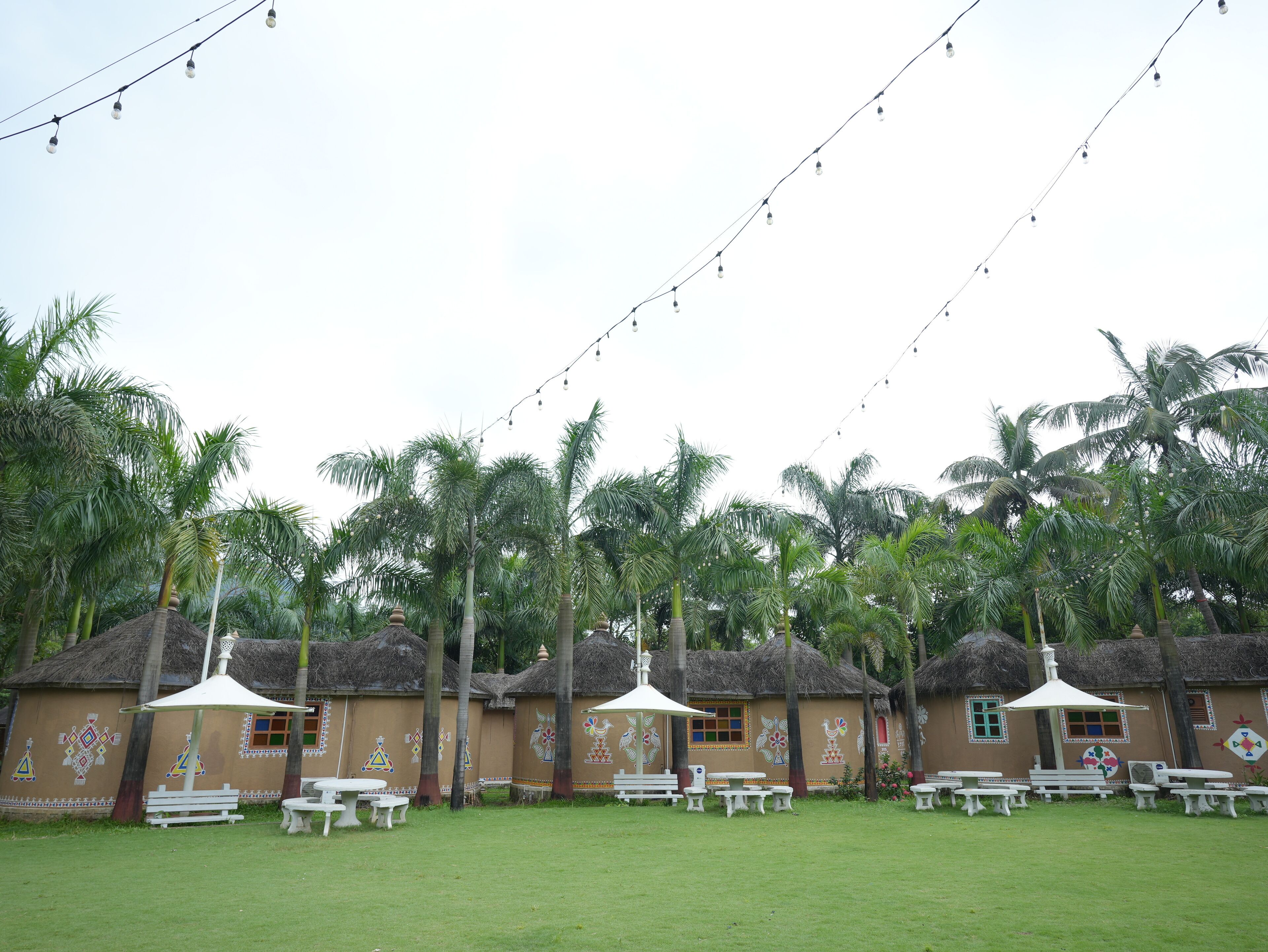 A tropical resort with thatched-roof huts, outdoor seating, and string lights.