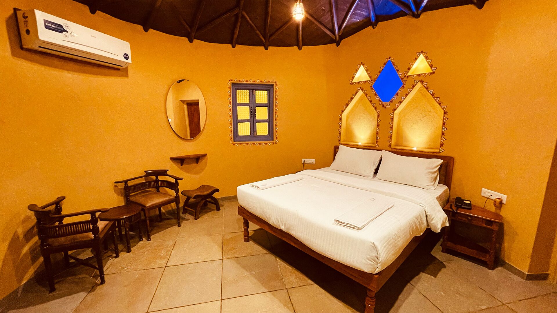 Une chambre d’hôtel comprenant un lit, une chaise, une petite table, un miroir et une fenêtre ornée d’un cadre décoratif.