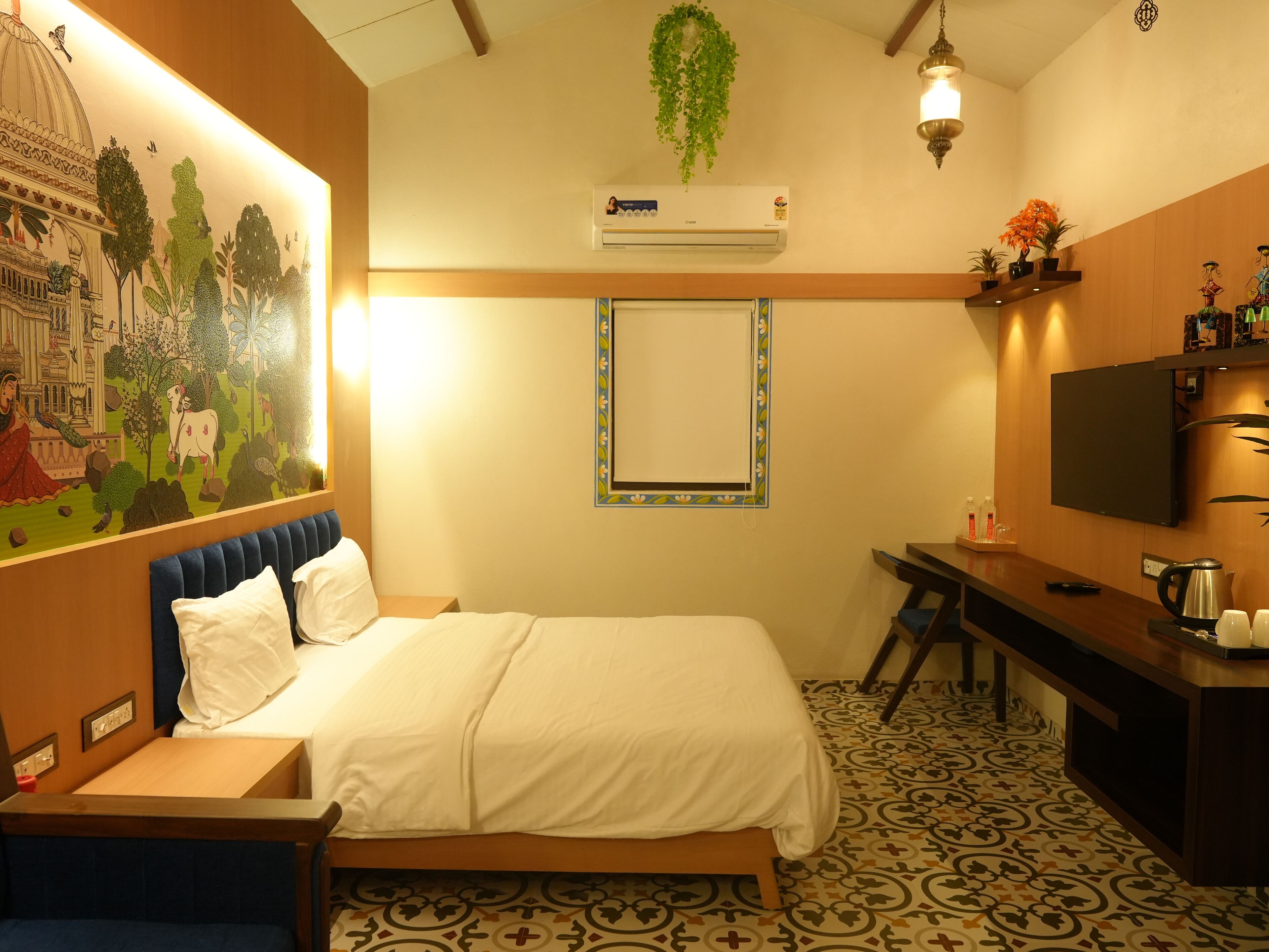 A hotel room with a bed, a desk, a TV, an air conditioner, and a decorative mural.