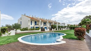 A residential building with a swimming pool, surrounded by a wooden deck and greenery.