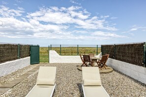 Una terraza con sillones, una mesa y sillas, rodeada por una valla y vistas al paisaje.