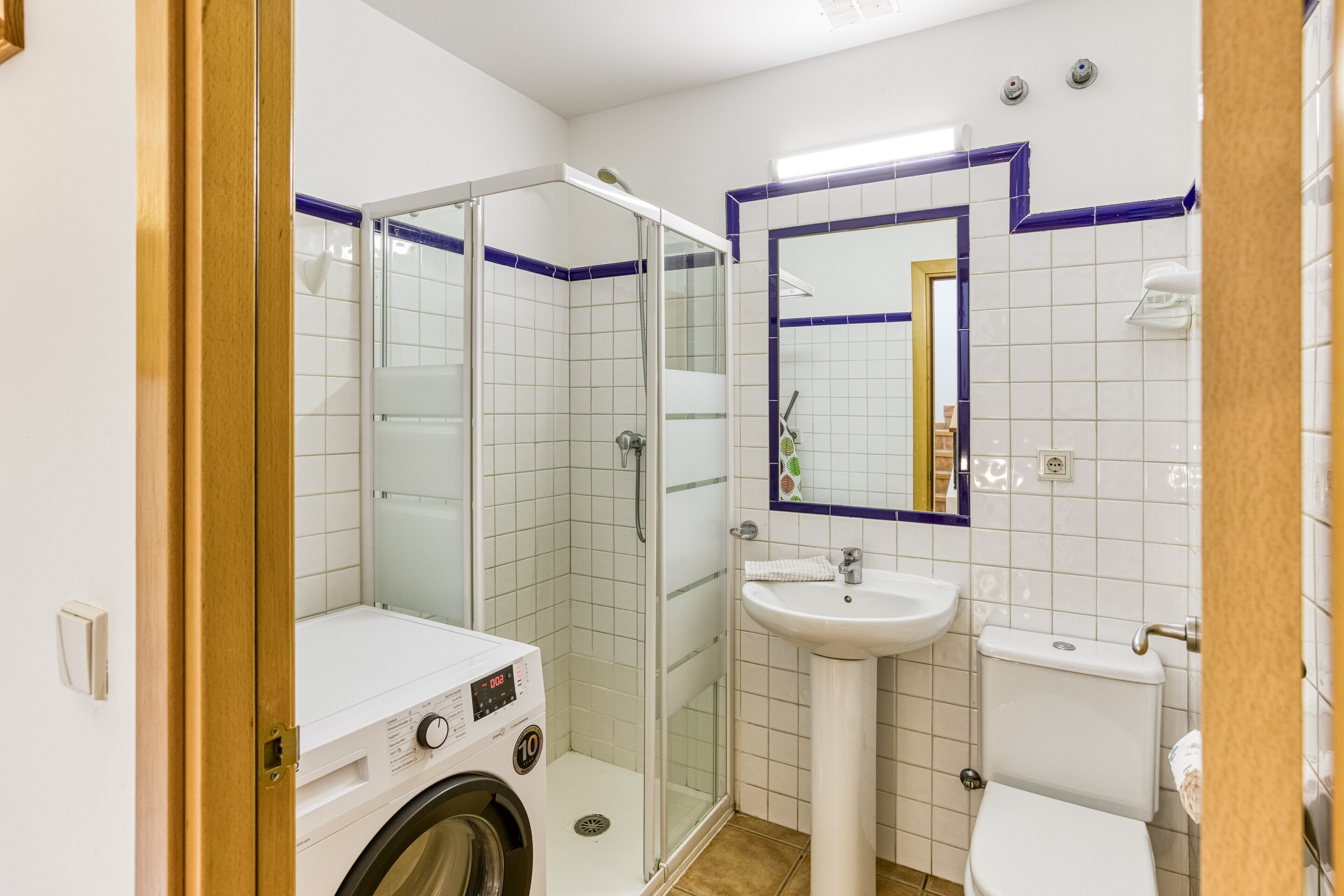 Un bagno con doccia vetrata, lavatrice, lavandino e water.