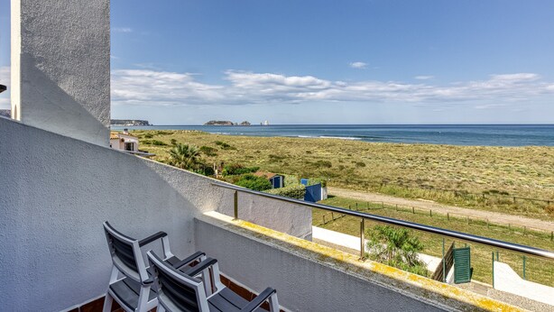 A balcony with chairs, a railing, and a view of the beach and ocean.
