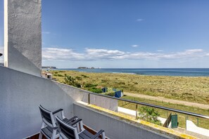 Een balkon met stoelen, een hekwerk en uitzicht op het strand en de zee.
