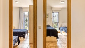A mirrored view of a room with two beds, a window, and a door leading to another room.