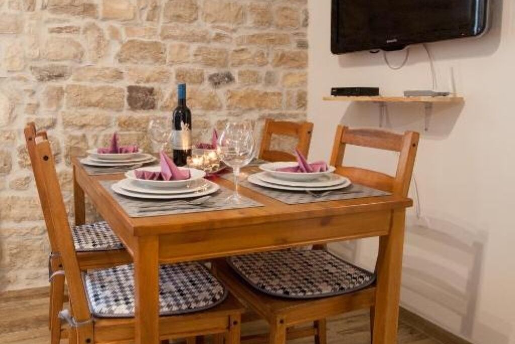 A dining table set with plates, glasses, and a bottle, surrounded by wooden chairs with patterned cushions.