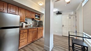 A kitchen with wooden cabinets, a stainless steel refrigerator, a microwave, and a glass dining table.