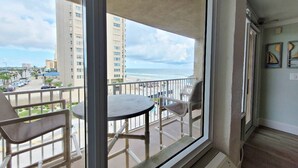 A balcony with a table and chairs, overlooking a beach and cityscape.