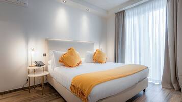 A modern hotel room with a large bed, a bedside table with a lamp, and a window with curtains.