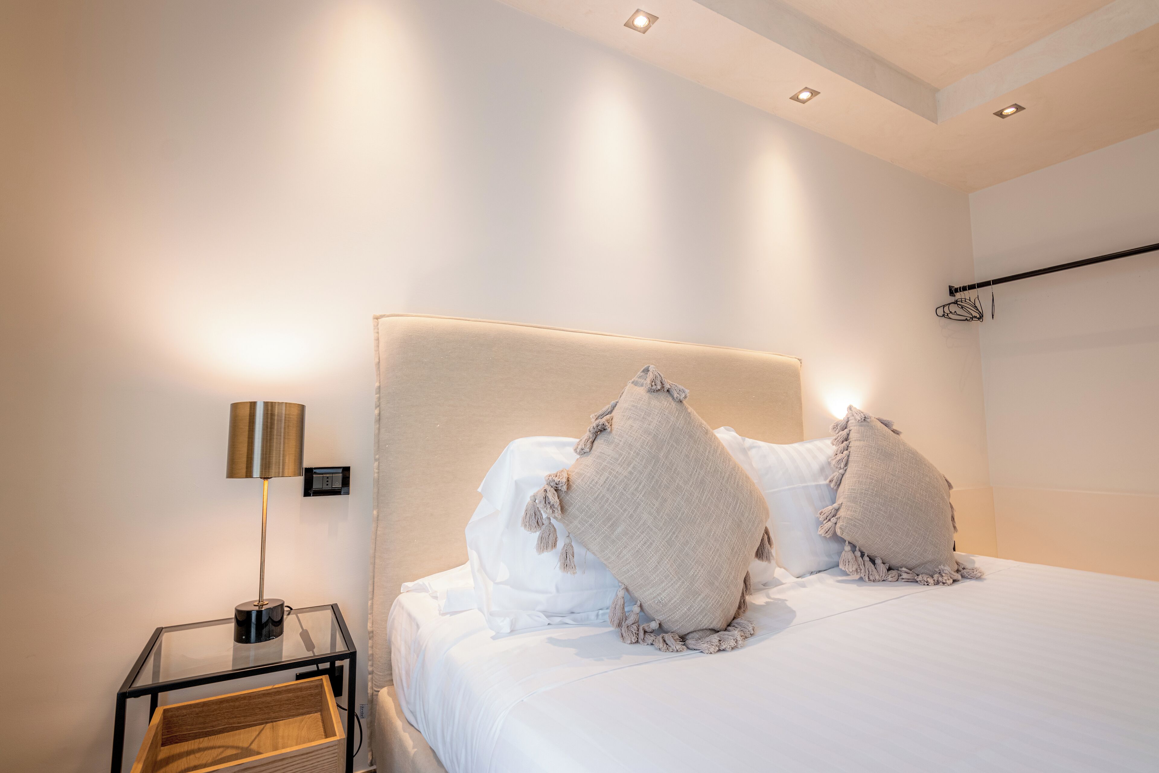 A modern bedroom with a large bed, a bedside table with a lamp, and a wall-mounted towel rack.