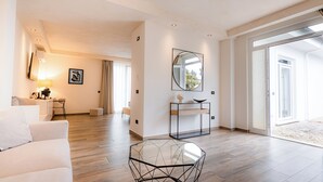 Een moderne woonkamer met een glazen salontafel, een bank, een bureau met een lamp, een grote spiegel en een schuifpui naar een balkon.