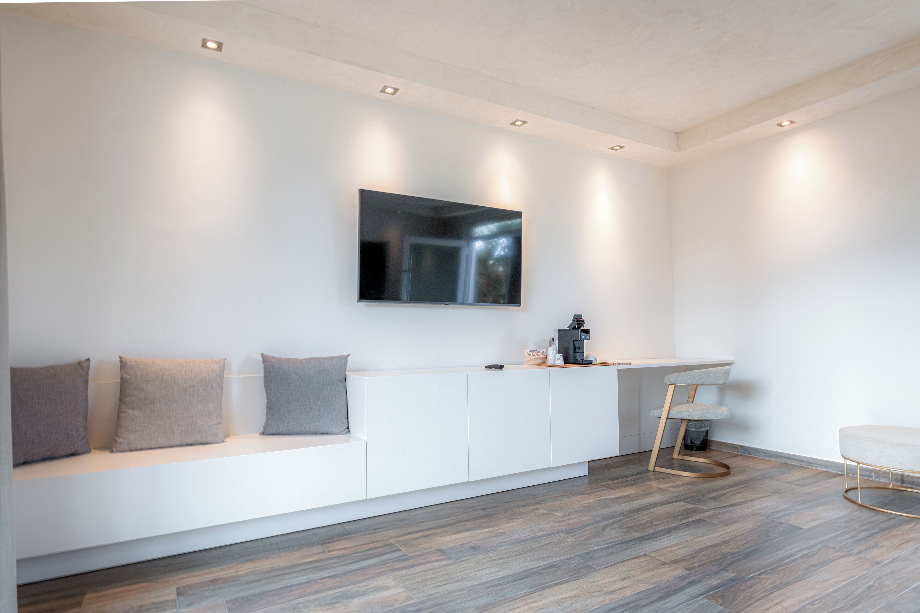A modern, minimalist living room with a white sofa, a coffee machine, and a TV mounted on the wall.