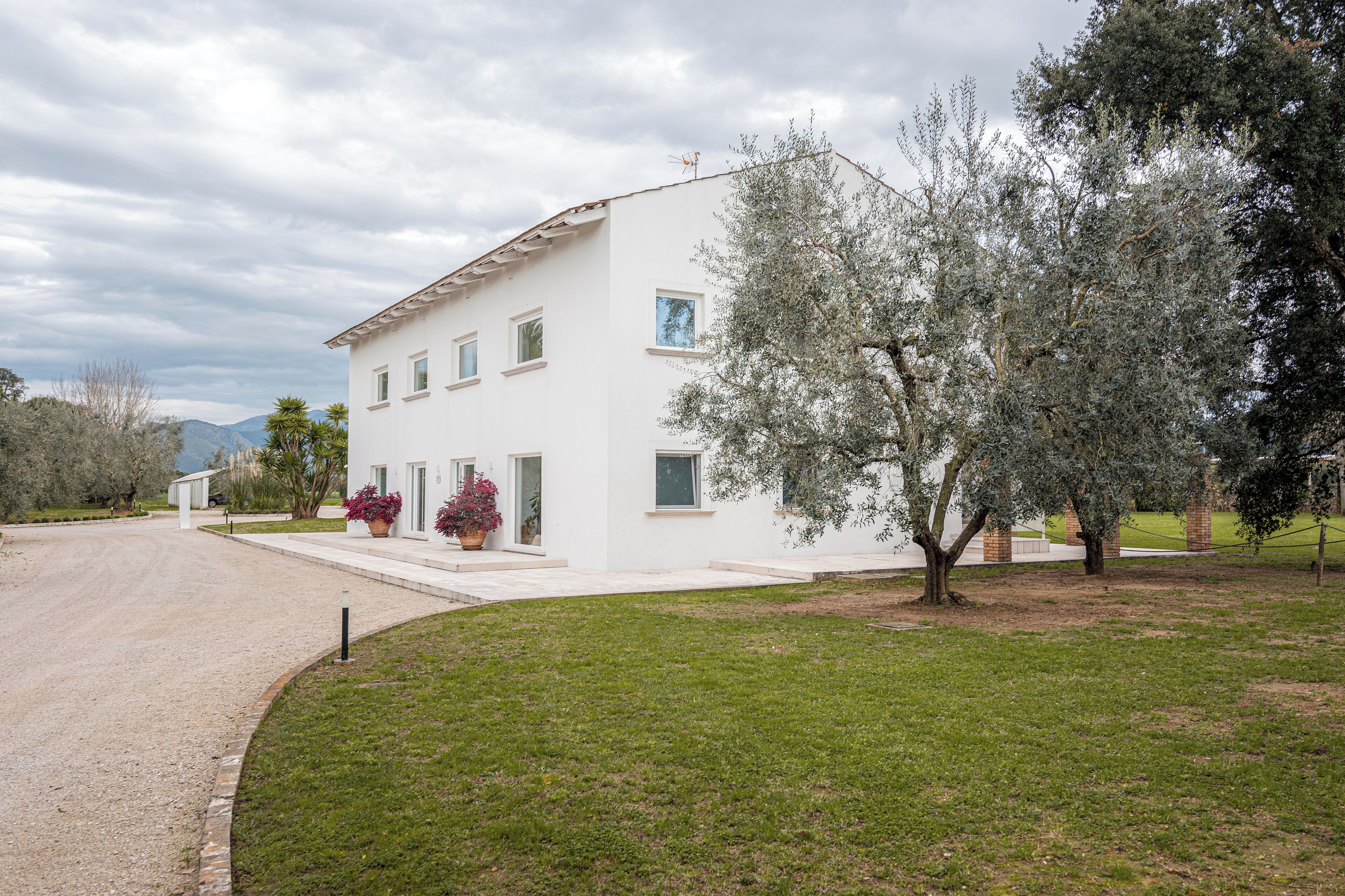 A two-story white building with a flat roof, a driveway, and a well-maintained lawn with trees.