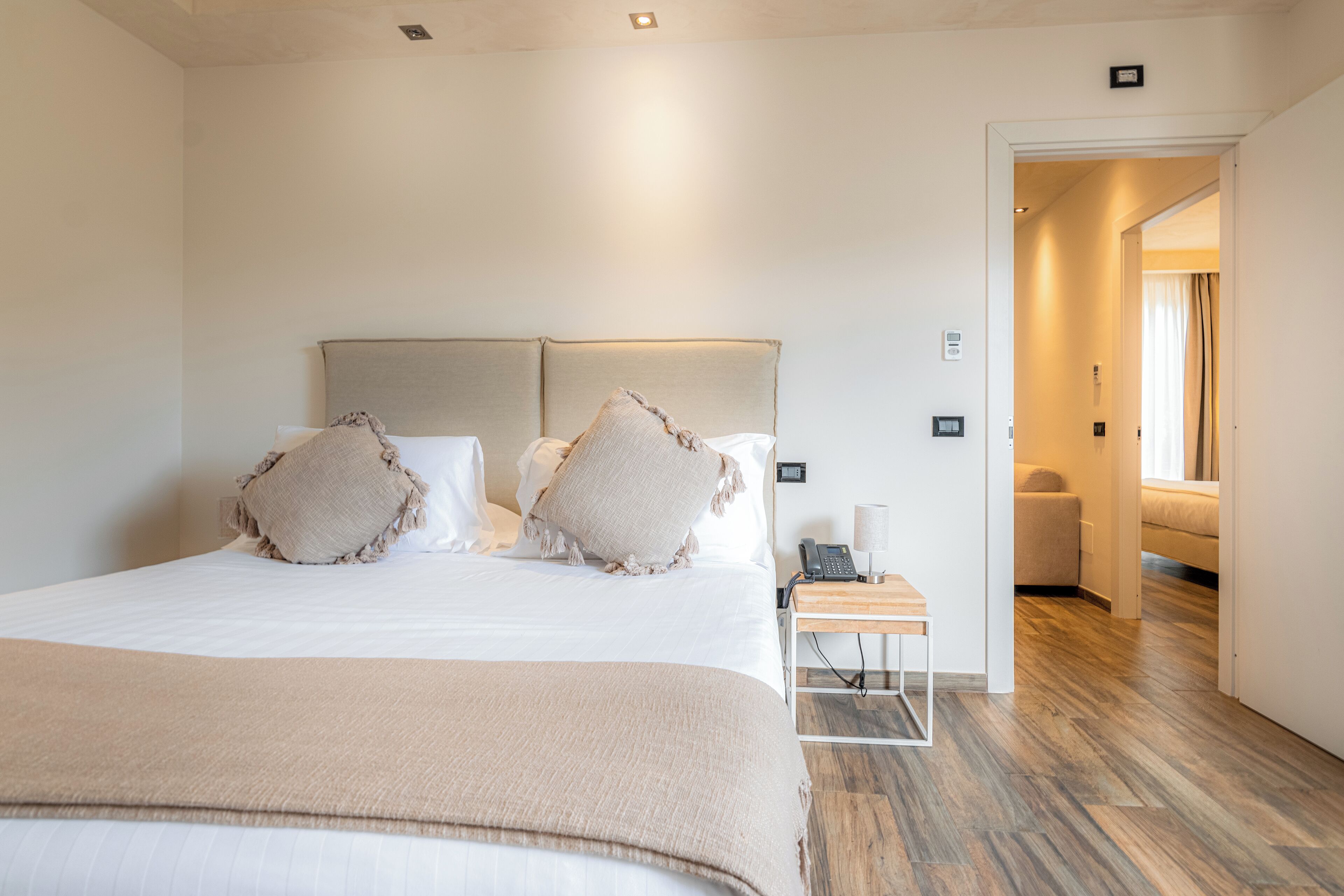 Quarto de hotel com uma cama grande, mesa de cabeceira e uma luminária.
