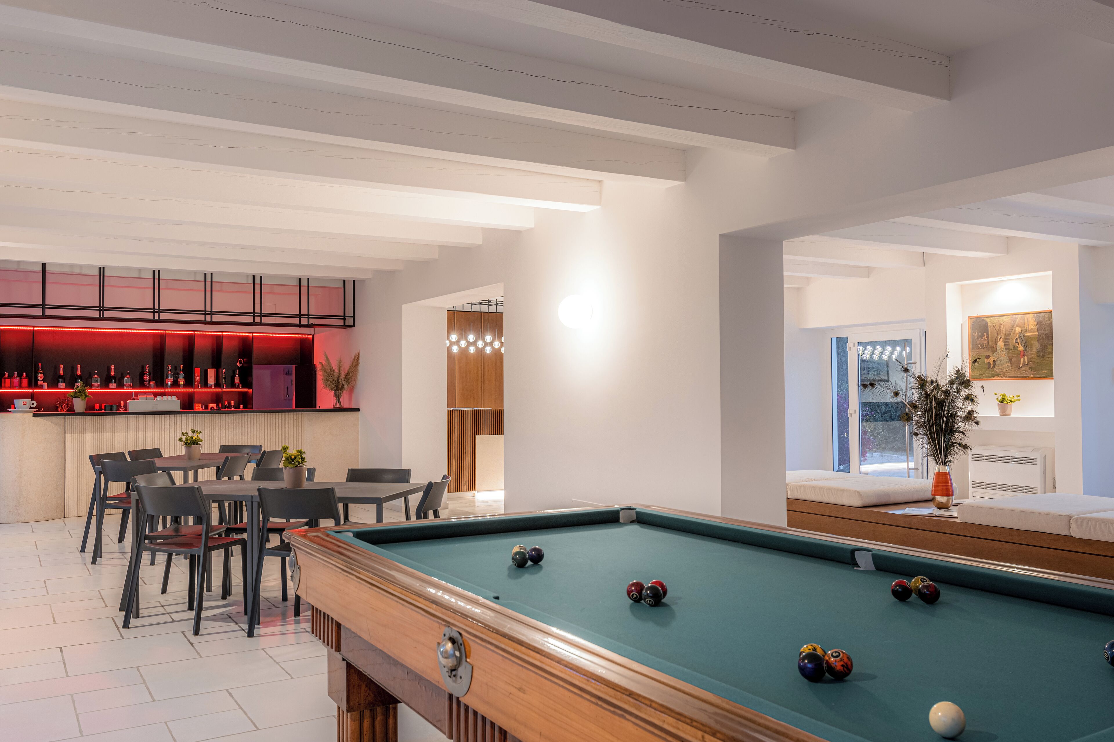 A pool table with balls, a bar area with red lighting, and a seating area with a sofa and chairs.