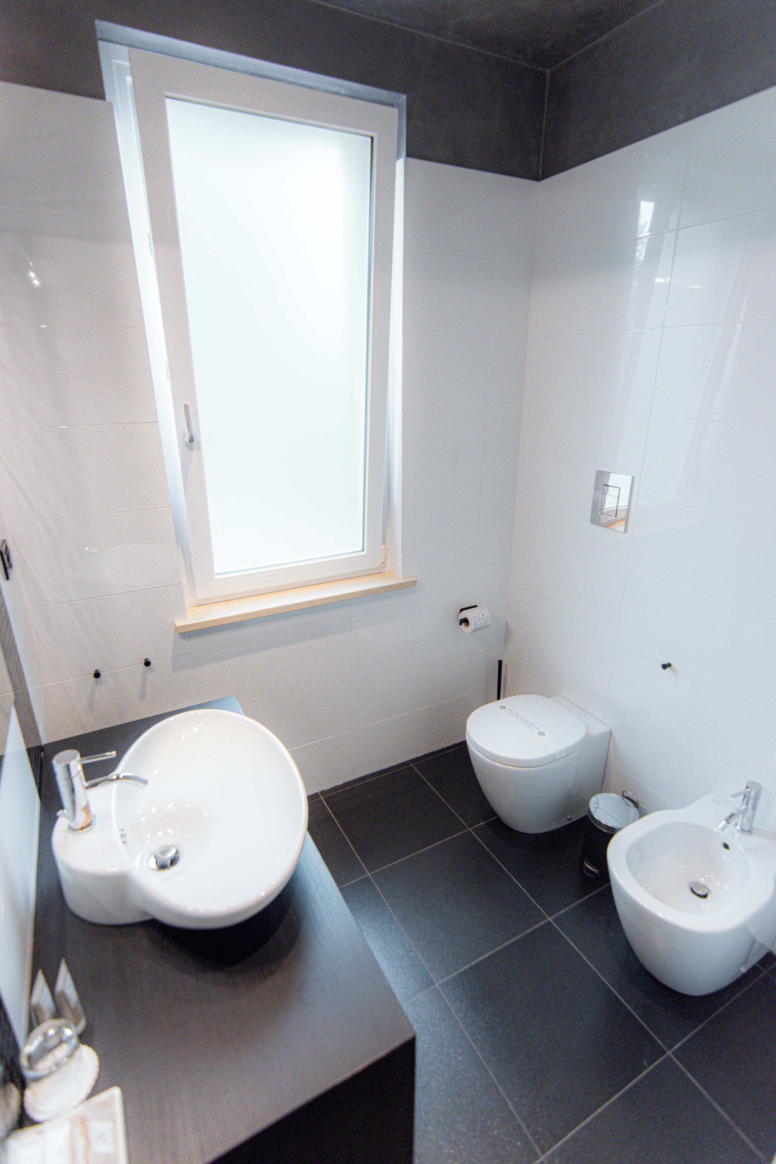 Une salle de bain moderne avec une grande fenêtre, un lavabo, un bidet et un miroir.