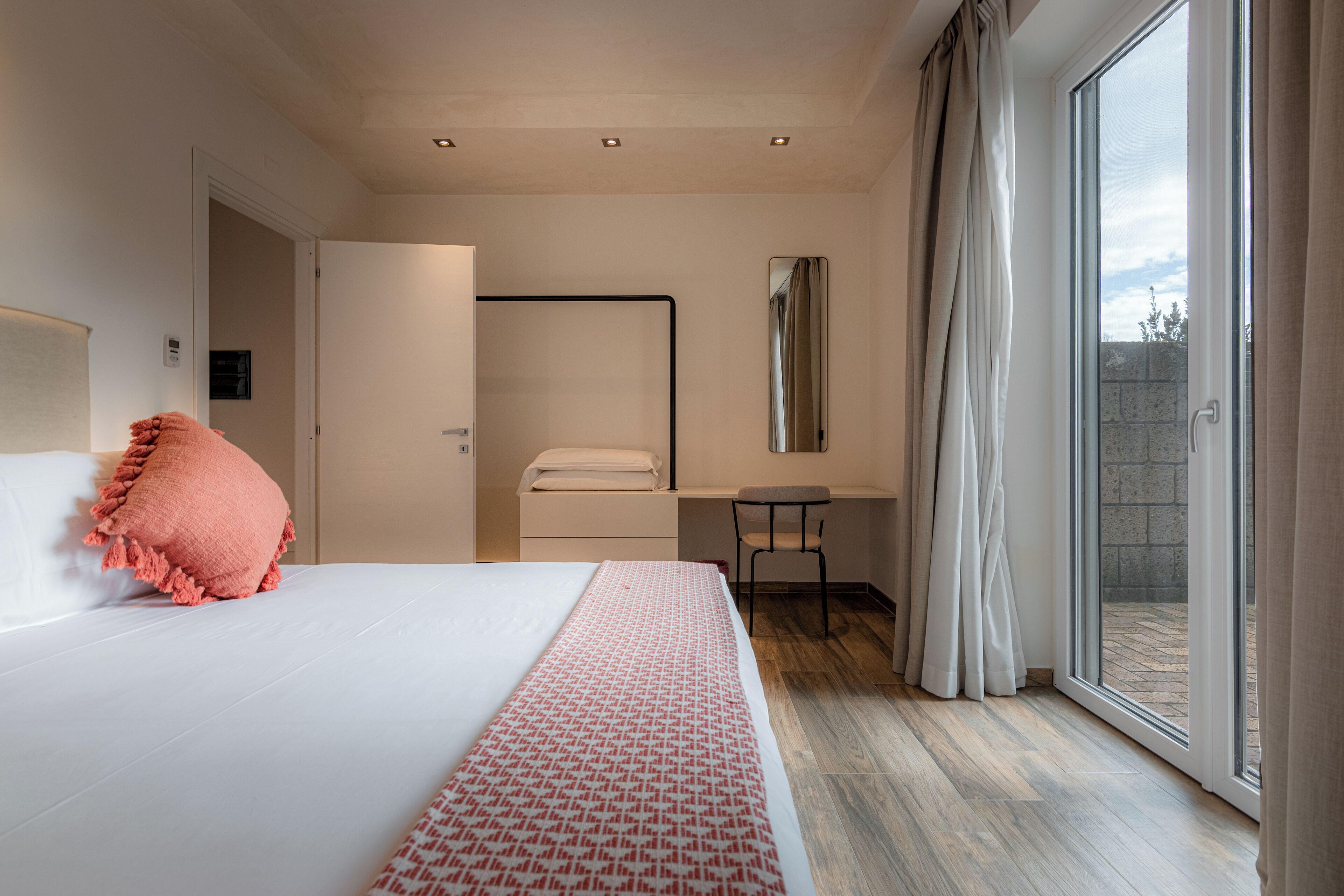 A modern hotel room with a large bed, a desk, and a sliding glass door to the outside.
