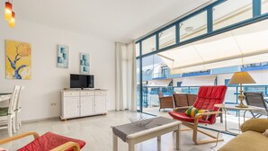 Un salon moderne doté d’un téléviseur, d’un coin repas et d’un balcon offrant une vue sur les immeubles.