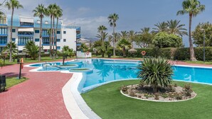 Une piscine entourée d’un jardin, de palmiers et d’un bâtiment à la façade bleue et blanche.