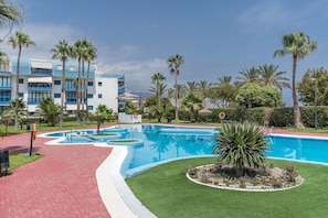 Une piscine entourée d’un jardin, de palmiers et d’un bâtiment à la façade bleue et blanche.