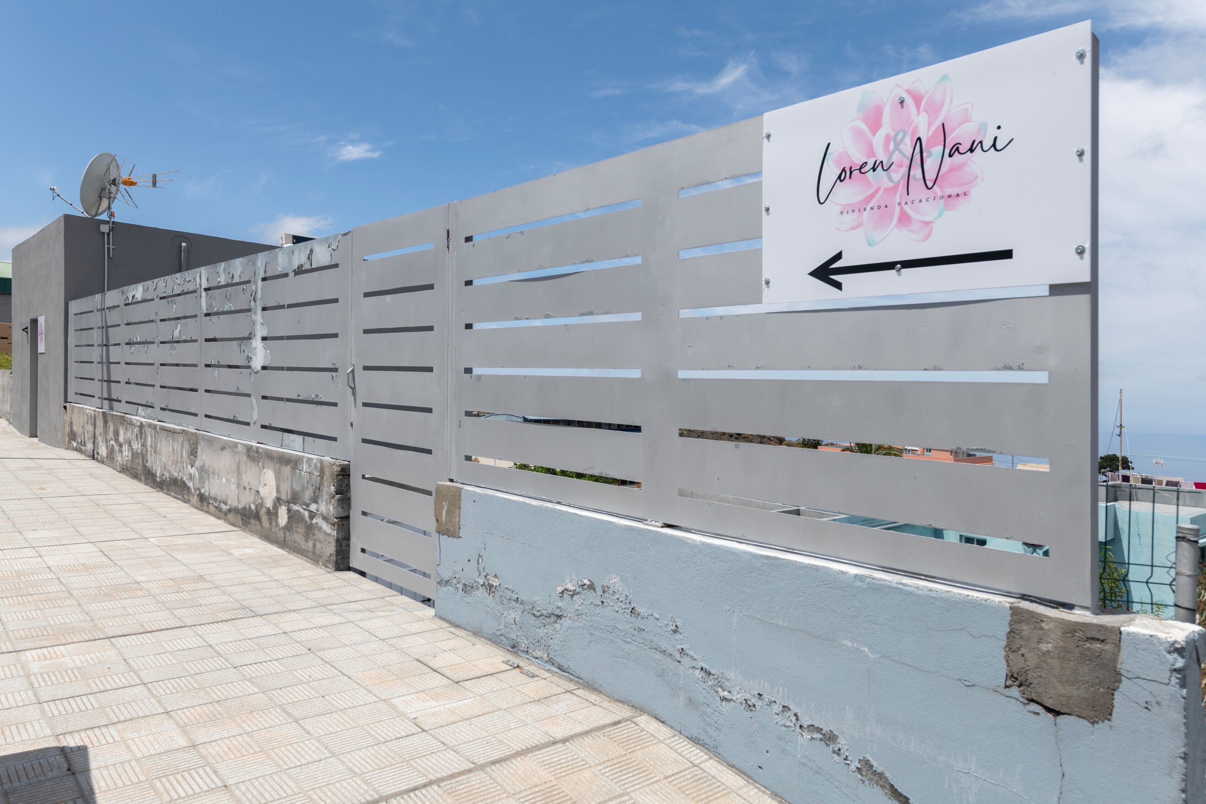 A white metal fence with a signboard indicating 'Loren & Nani' and an arrow pointing left.